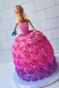 a barbie doll sitting on top of a pink and purple cake