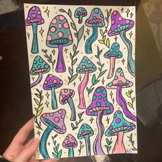 a hand holding up a piece of paper with colorful mushrooms on it