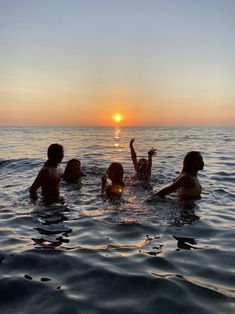 four people in the water at sunset with one person raising their hand up to the sky