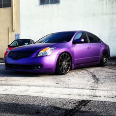 a purple car parked in front of a white building next to another red and blue car