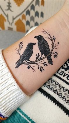 two black birds sitting on top of a branch with leaves and branches around it's neck