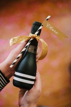 a person holding a wine bottle with a straw in it and a gold ribbon on top