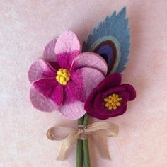 three felt flowers are tied together on a pink surface