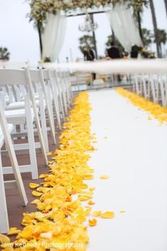 the aisle is lined with white chairs and yellow petals