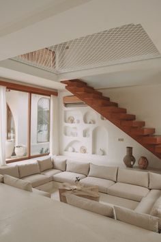 a living room filled with white furniture next to a wooden bannisti stair case