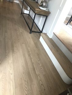 a wooden floor with white trim and wood stairs in the background, next to a table with vases on it