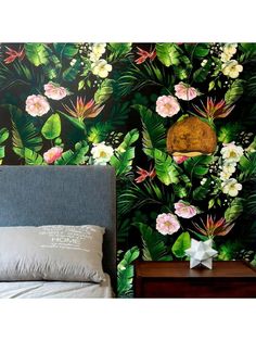 a bed sitting next to a wall covered in green leaves and pink flowers on top of it