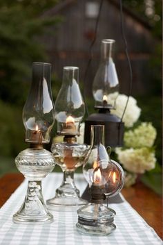 three glass vases sitting on top of a white tablecloth covered table with flowers in the background