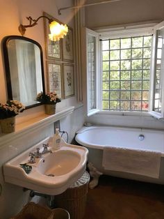 a bath tub sitting next to a sink under a bathroom window with a mirror above it