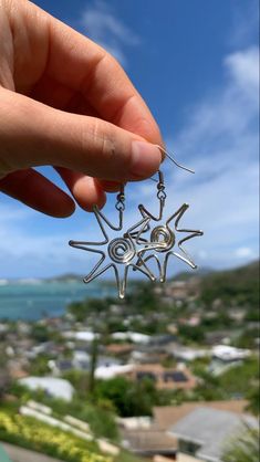 a person is holding up a small silver star ornament in front of the ocean