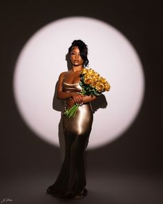 a woman in a gold dress holding flowers and posing for a photo with a white circle behind her