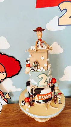 a birthday cake with toy figures on the top and bottom tier, sitting in front of a cartoon wall