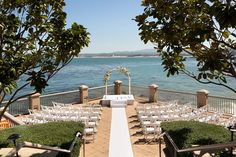 an outdoor ceremony set up by the water with white chairs and greenery on either side