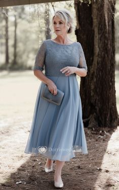 an older woman in a blue dress standing under a tree with her hand on her hip