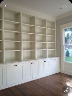 empty white bookcases in the corner of a room with wood floors and windows