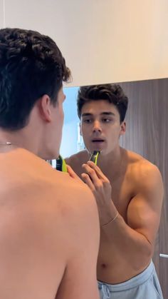 a young man brushing his teeth in front of a mirror while looking at himself in the mirror