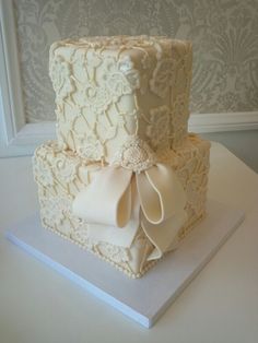 a wedding cake with white lace and bows on it's tiered square shape