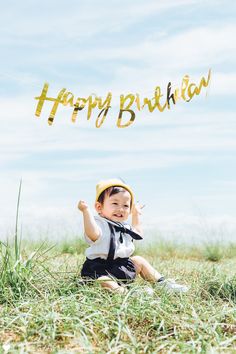 a little boy sitting in the grass holding up a happy birthday sign