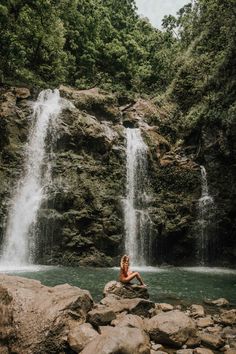 a woman sitting on rocks in front of a waterfall