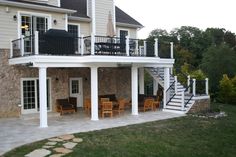 a patio with chairs and tables in front of a large house that has stairs leading up to the second floor