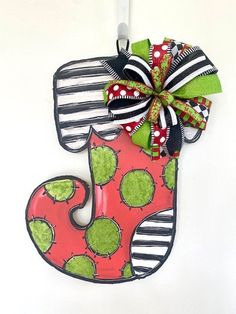 a red and green christmas stocking hanging from a hook on a white wall with a bow