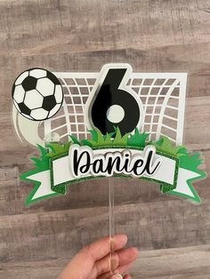 someone is holding up a cake topper with a soccer ball and goal on it