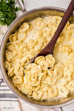 a skillet filled with pasta and sauce on top of a white table cloth next to a wooden spoon