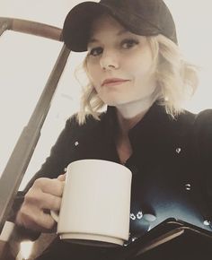 a woman holding a coffee cup in her right hand and wearing a black hat on top of her head