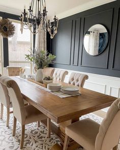 a dining room table with chairs and a mirror on the wall above it, in front of a chandelier