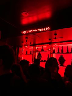 a group of people standing in front of a red lit room with bottles on the wall