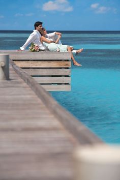 a man and woman sitting on a dock next to the ocean