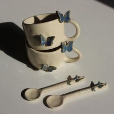 two cups and spoons with blue butterflies on them, sitting next to each other