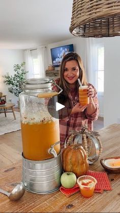 a woman is holding a glass in front of a jar filled with liquid and pumpkins