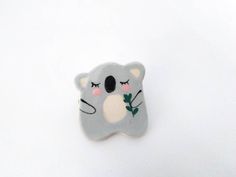 a koala bear brooch sitting on top of a white surface with its eyes closed