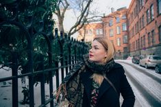 a woman standing next to a fence in front of some buildings on a snowy day