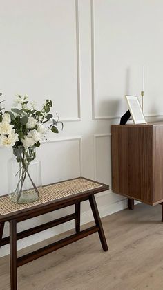 a vase with white flowers sitting on a table next to a wooden cabinet and sideboard