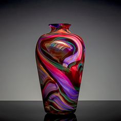 a colorful glass vase sitting on top of a black table next to a gray wall