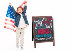 a little boy holding an american flag and standing next to a sign that says, this is going to be a big brother january 22