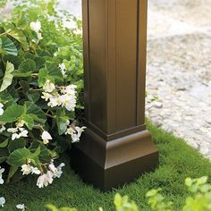 a clock is sitting in the grass next to some bushes and flowers on the ground