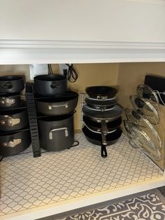 pots and pans are stacked on the floor under a shelf in a room with carpeting