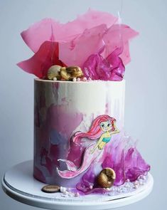 a pink and white cake decorated with mermaid decorations