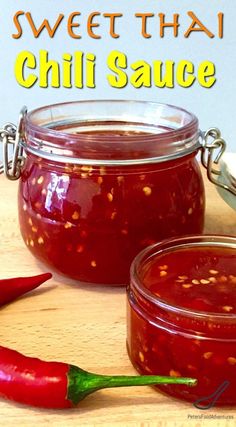 two jars filled with chili sauce sitting on top of a wooden table