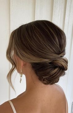 a woman with her hair in a low bun, wearing gold earrings and a white tank top