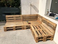 a wooden bench made out of pallets sitting on the side of a building next to a window