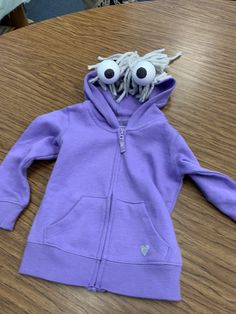 a purple jacket with eyes and ears on it sitting on top of a wooden table