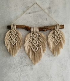 three macrame tassels hanging from a wooden stick on a concrete wall