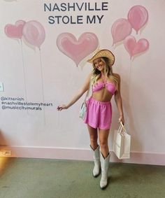 a woman standing in front of a pink wall with balloons on it and a hat over her head