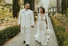 a bride and groom walking down a path holding hands