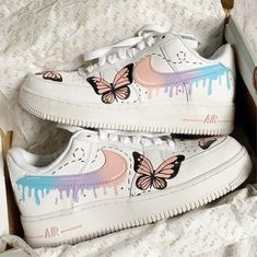 a pair of white shoes with pink and blue butterflies painted on them, sitting in a box