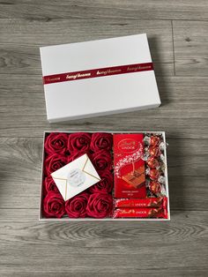 an open box with red roses and chocolates on the inside, sitting on a wooden surface